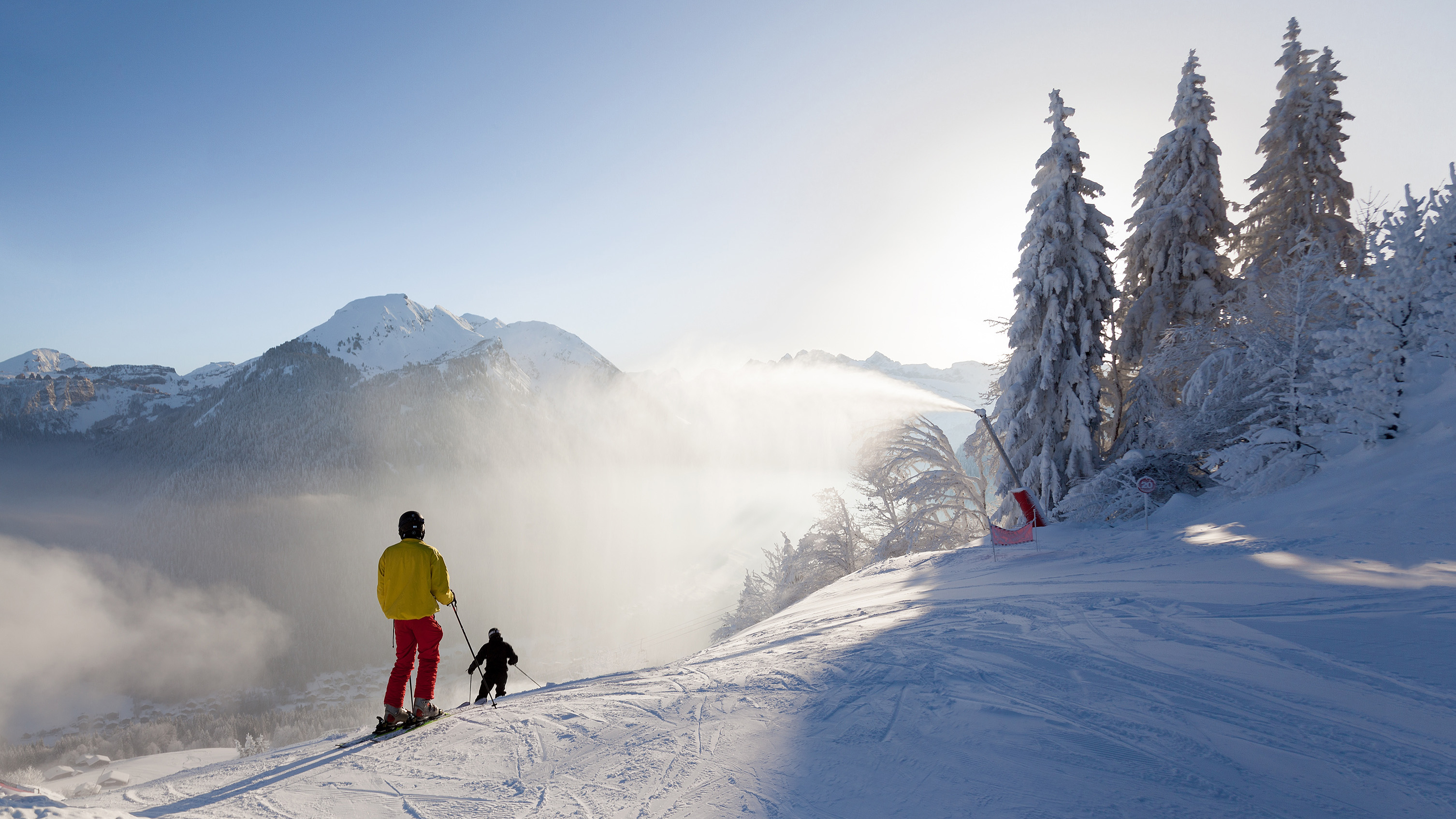 2 skiers heading down an isolated mountain pass at low light with fog.